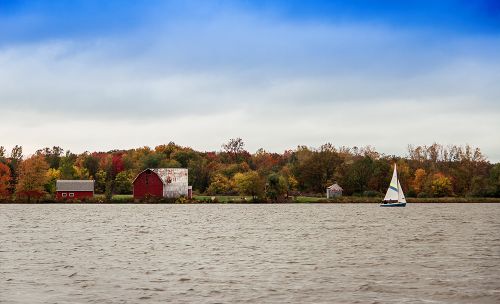 The image is of Mott lake in Flint. On the shore in the distance is a small sailboat and a red barn.