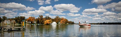 The image is of Fall Lake. The sky is blue with clouds overlooking the lake with a boat floating by.