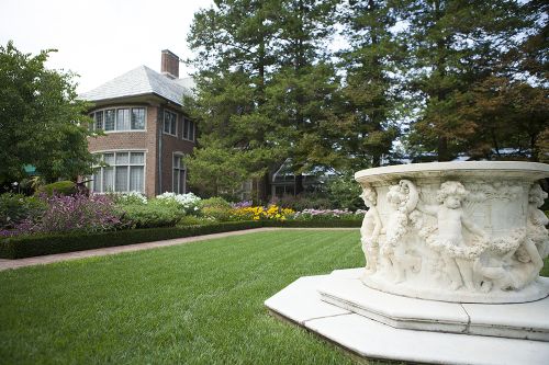 The image is of Applewood. There is green grass with a fountain with statues around it and a house off in the distance. 