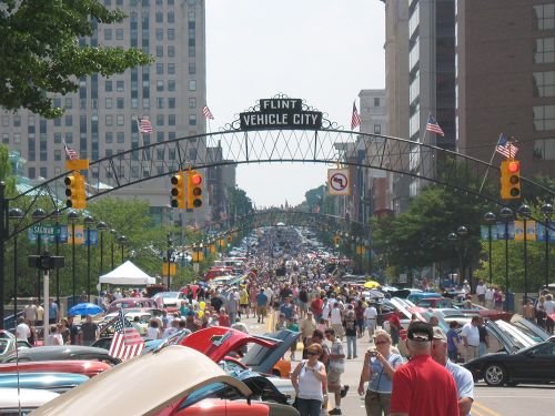 The image is on the Flint vehicle city sign with American flags with buildings behind.  