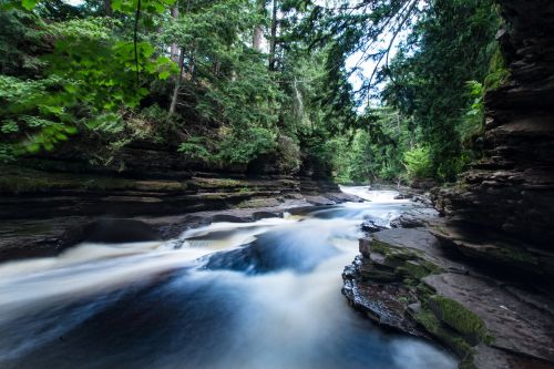 The image is of flowing water down the Manabezho Falls. Surrounded by rocky platforms with a forest of trees around.